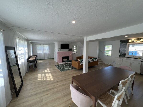 A modern living room with a wooden dining table, a sofa, and a TV mounted on the wall.