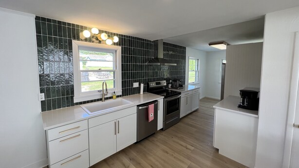Una cocina moderna con armarios blancos, salpicadero negro y ventana con vistas al exterior.