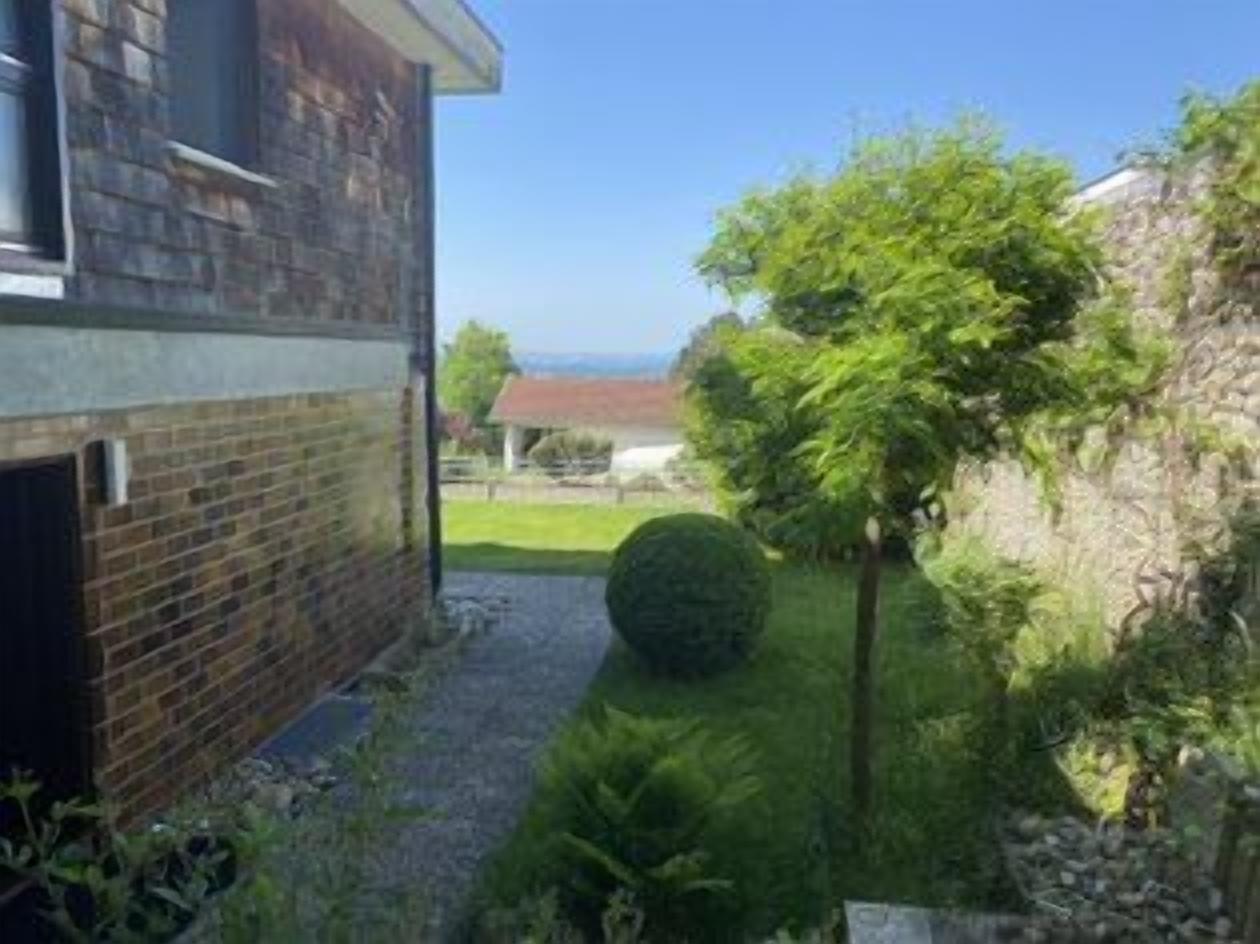 A residential property with a brick exterior, a paved driveway, and a well-maintained garden with a hedge and a spherical topiary.