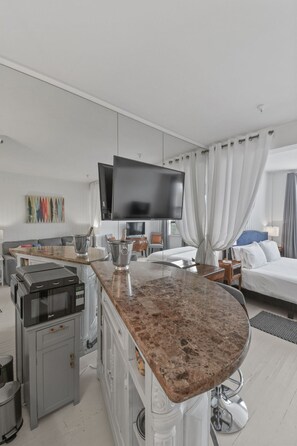 Habitación de hotel moderna con cocina, televisor de pantalla plana, cama con dosel y mesa de comedor.