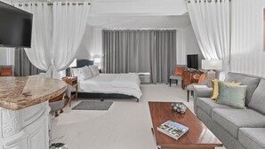 A hotel room with a bed, a TV, a sofa, a coffee table, and a desk with a chair.