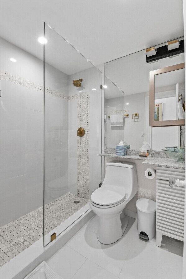 Un baño moderno con ducha envuelta en vidrio, inodoro, lavamanos y espejo.