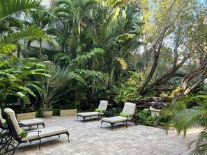 Un patio con cuatro sillones de descanso y una pequeña mesa, rodeado de exuberante vegetación tropical y árboles.