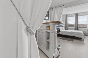 Una habitación de hotel moderna con cama, un mueble bajo y vistas amplias por las ventanas.