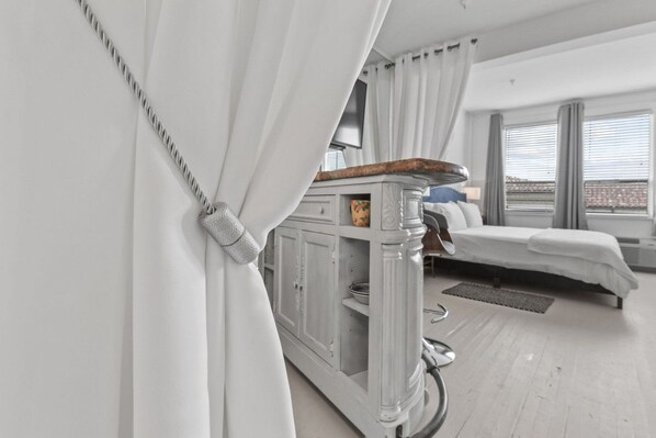 Una habitación de hotel moderna con cama, un mueble bajo y vistas amplias por las ventanas.