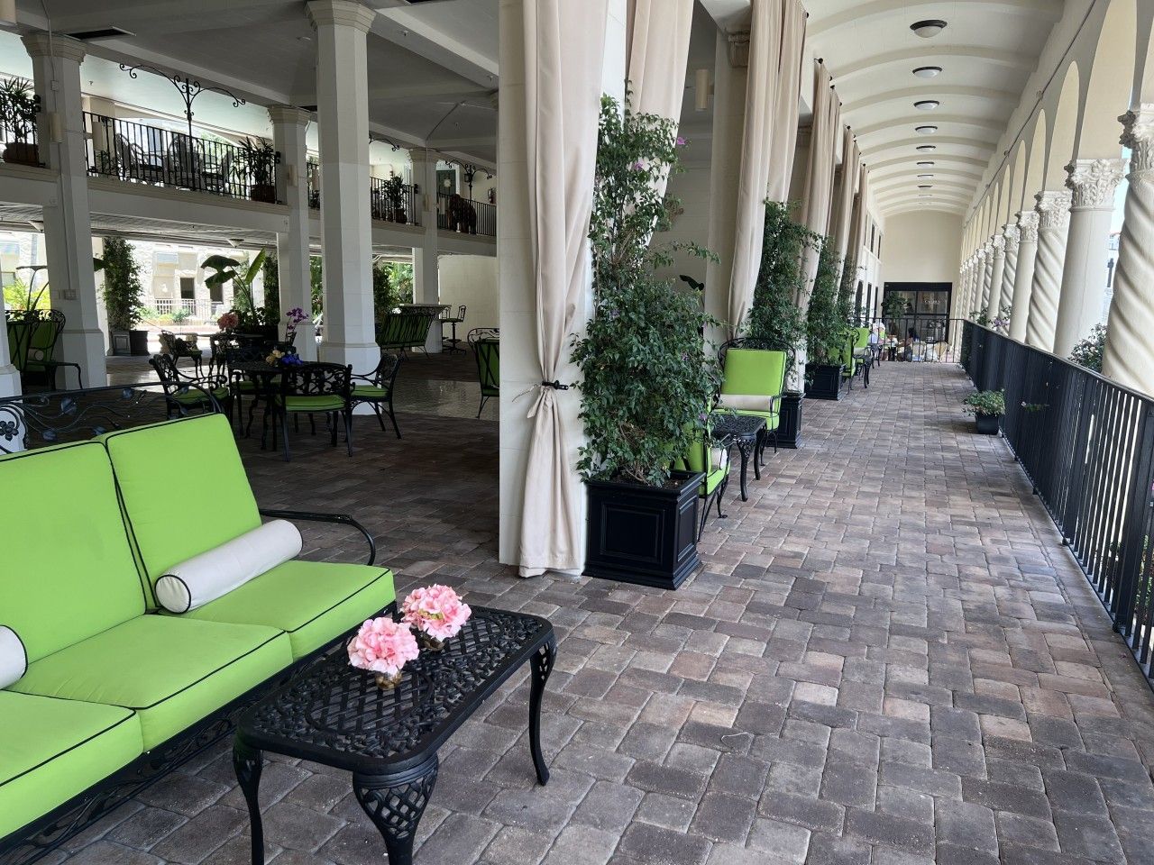 A covered outdoor seating area with green sofas, a table with flowers, and potted plants.