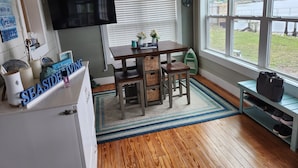 Una cocina funcional con una mesa de madera, un televisor montado encima y vistas a un lago a través de amplios ventanales.