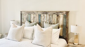 A bed with white bedding and multiple pillows, a rustic wooden headboard, and two bedside lamps on a nightstand. - BRAND NEW! Whalehead Beach Mediterranean Inspired Villa (Corolla)