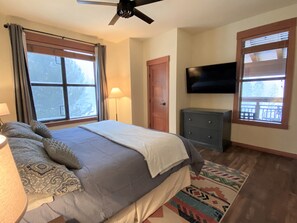 A bedroom with a bed, a TV, a dresser, and a window with curtains.