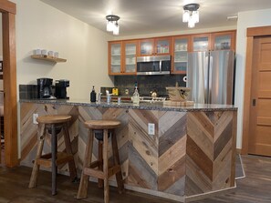Una cocina con salpicadero de diseño en espiga, electrodomésticos de acero inoxidable, taburetes de bar de madera y una estación de café.