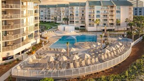 Un hotel con varios pisos, una piscina y una terraza con sillones de descanso.