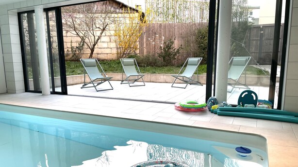 En pool med en flytande badring, två solstolar och utsikt över en trädgård med ett trästaket och träd.
