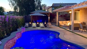 A backyard with a swimming pool, lounge chairs, and a covered patio area.