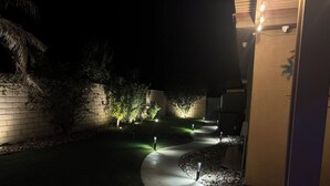 A nighttime outdoor pathway with illuminated ground lights, a brick wall, and a tree.