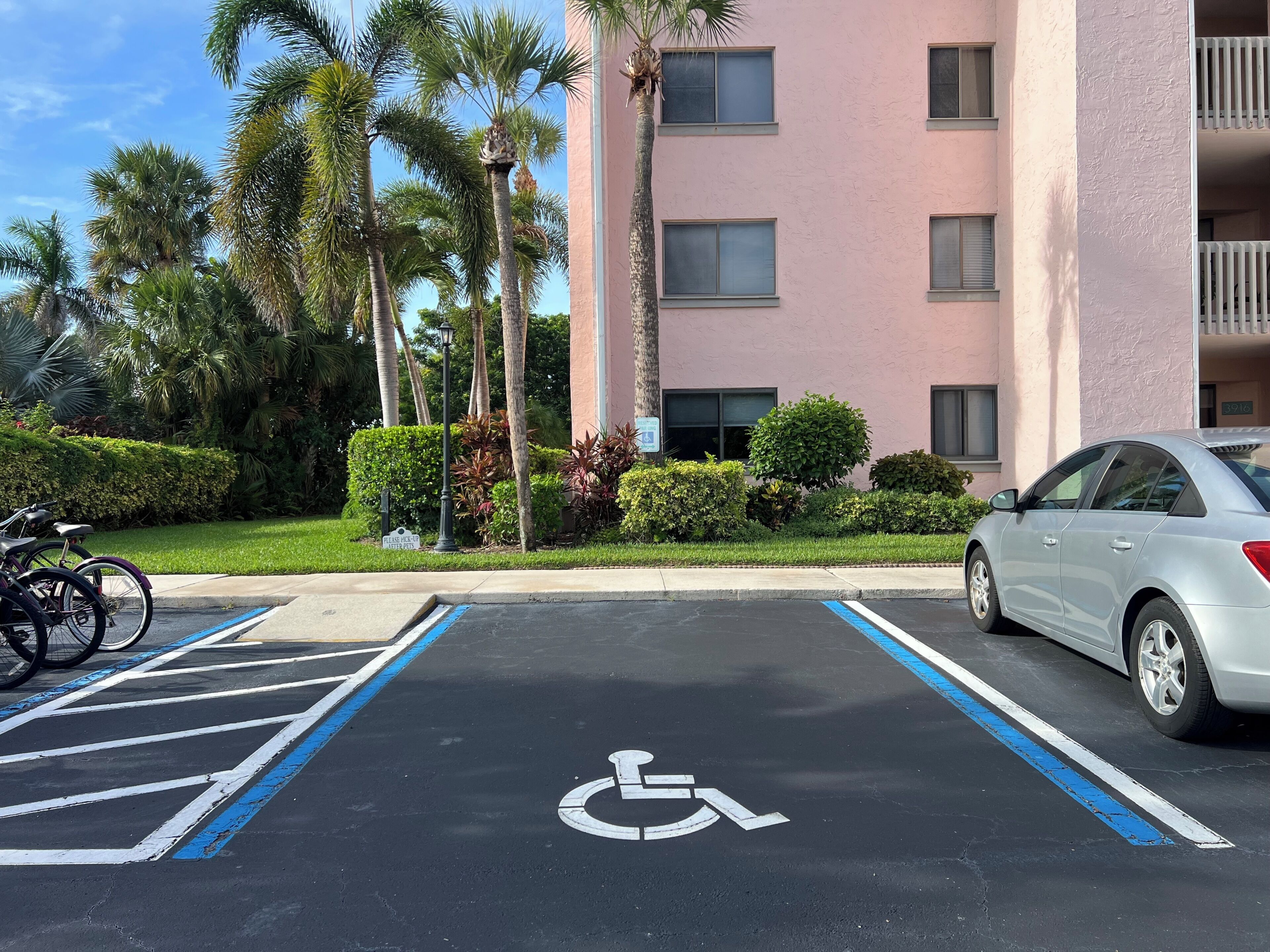 Un espace de stationnement comprenant une place réservée aux personnes handicapées, une voiture et un bâtiment doté de nombreuses fenêtres et de balcons.