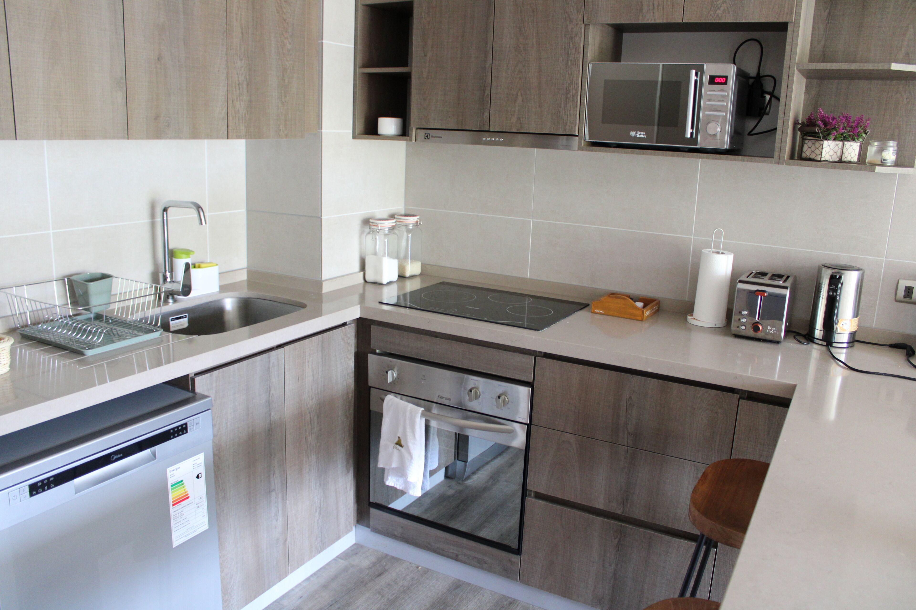 A modern kitchen with wooden cabinets, a stainless steel sink, a built-in microwave, a toaster, and a dishwasher.