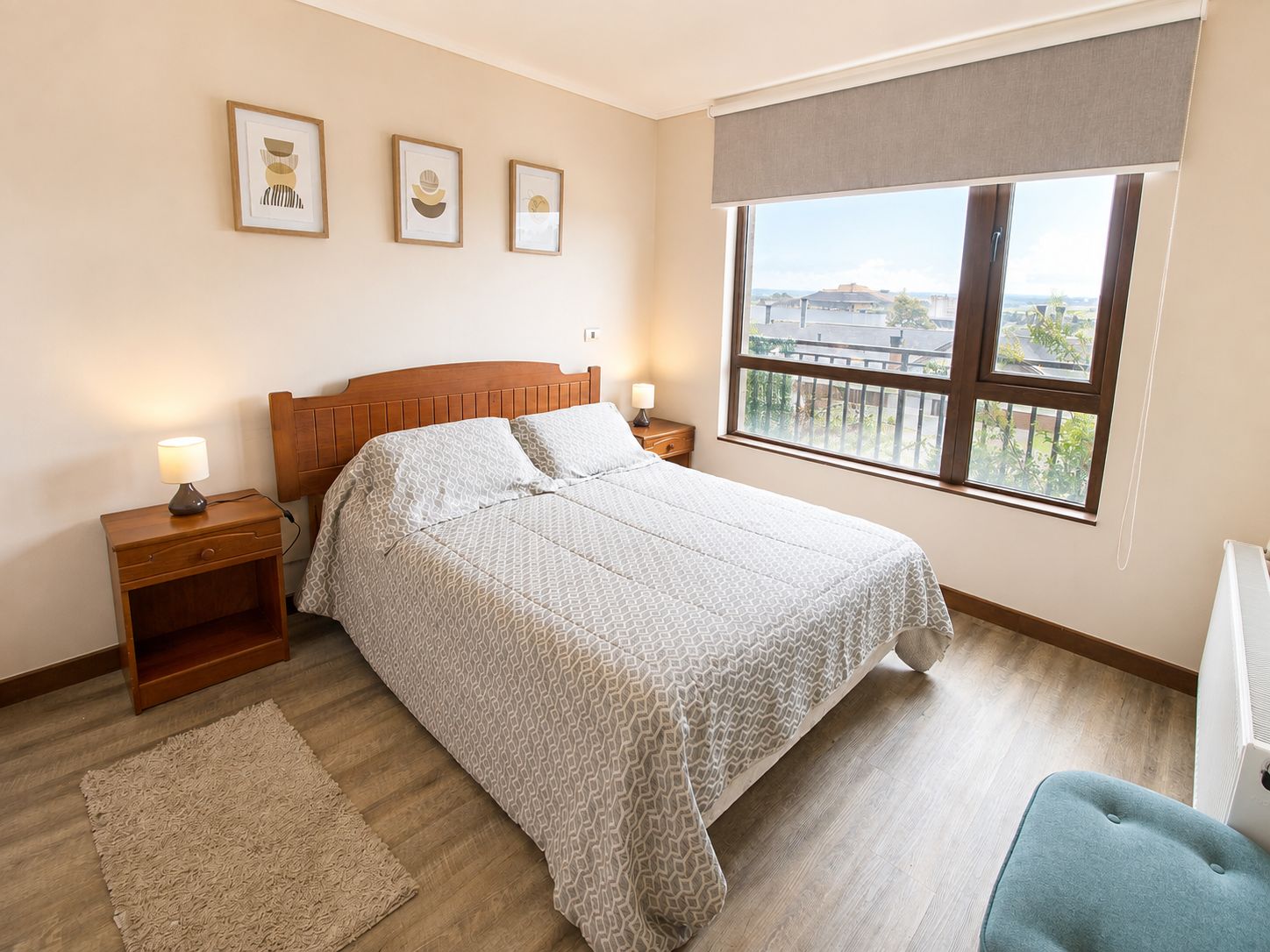 A bedroom with a bed, bedside tables, a window with a view, and framed pictures on the wall.