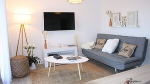 Una sala de estar moderna con un sofá gris, una mesa de centro blanca, un televisor de pantalla plana y una lámpara colgante.