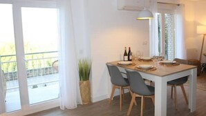 Un comedor con una mesa dispuesta para cuatro, una planta en maceta y vistas al exterior a través de una puerta corredera.