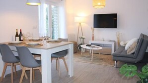 Una sala de estar moderna con comedor, sofá, televisor montado en la pared y una lámpara.