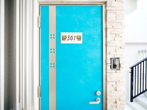 A blue door with a number plate, a metal handle, and a peephole.