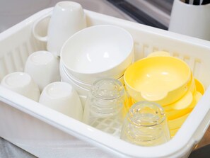 Un panier en plastique blanc contenant divers ustensiles de cuisine, notamment des bols, des tasses et des bocaux.