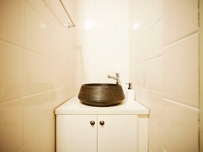 Une salle de bain avec un lavabo rond de couleur sombre, posé sur un plan de toilette blanc, un robinet chromé et un porte-rouleau de papier toilette.