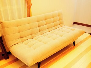 A sofa with a tufted backrest and armrests, positioned on a wooden floor.