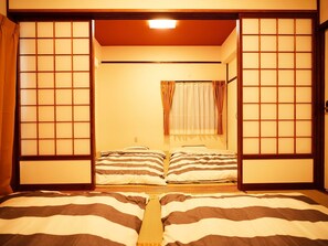 A traditional Japanese-style room with tatami flooring, a futon bed, sliding shoji screens, and a shoji door.