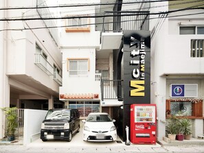 A building with a sign reading 'Mcity in Maejima' and a Coca-Cola vending machine.