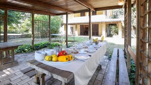 An outdoor dining area with a long table set for a meal, surrounded by wooden benches and a pergola structure. - Lovely home in Rivotorto di Assisi (Rivotorto di Assisi)