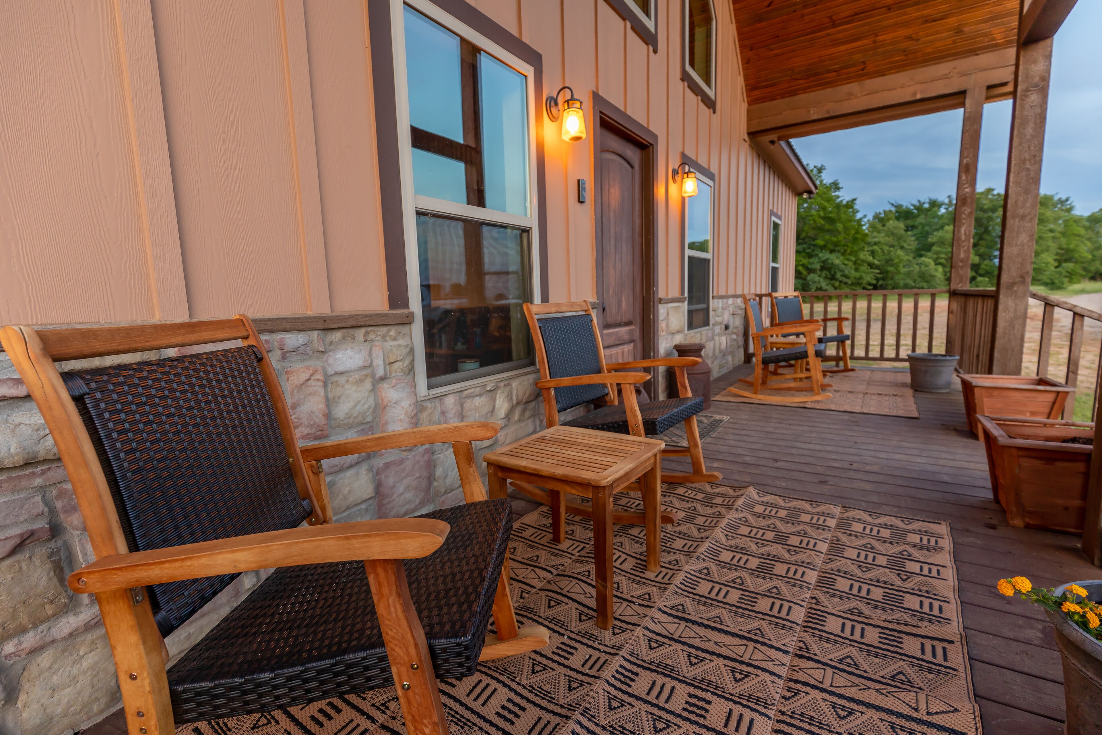 A wooden deck with outdoor furniture, including chairs and a table, and a patterned rug.