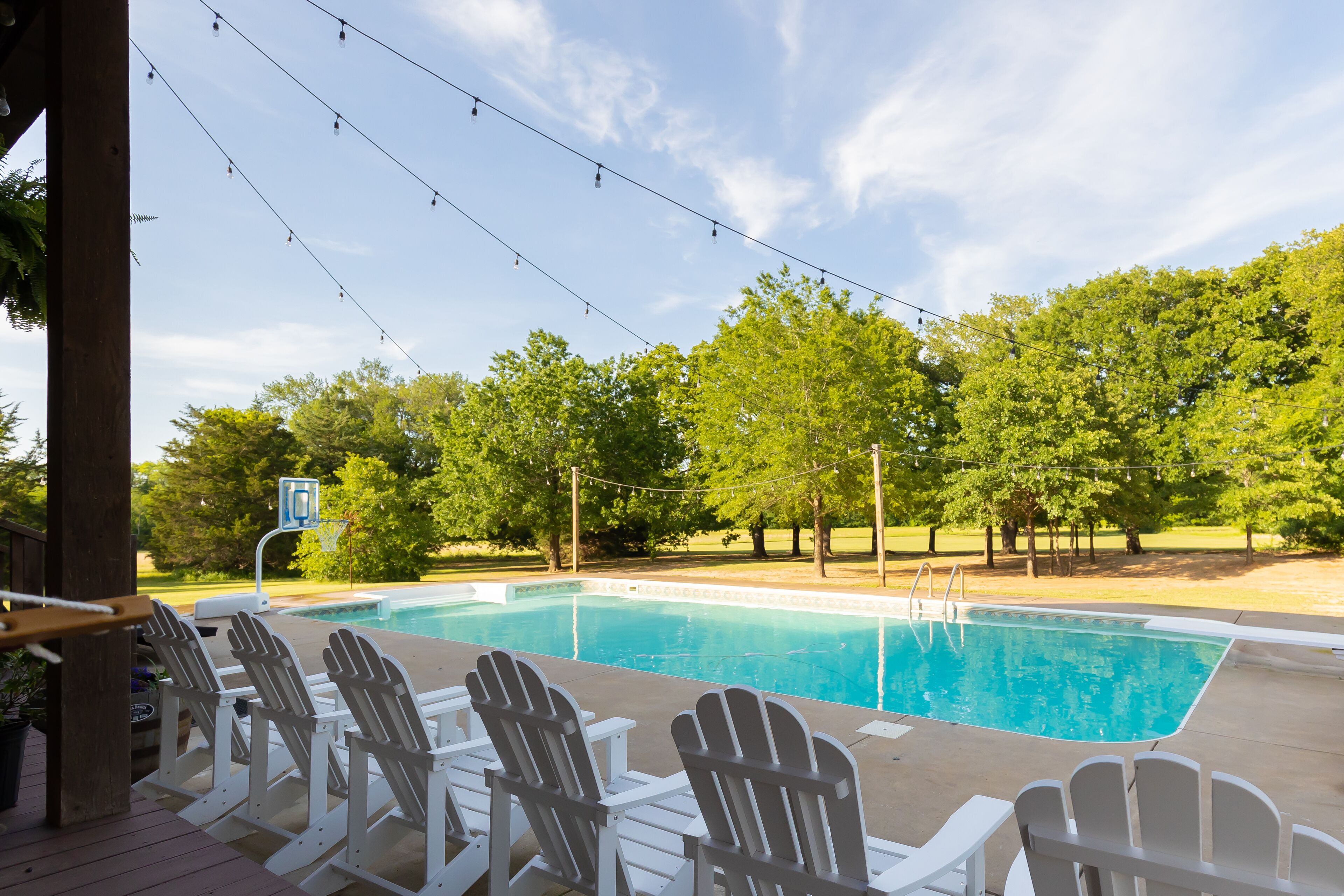 Una piscina con sillas Adirondack y luces colgantes.