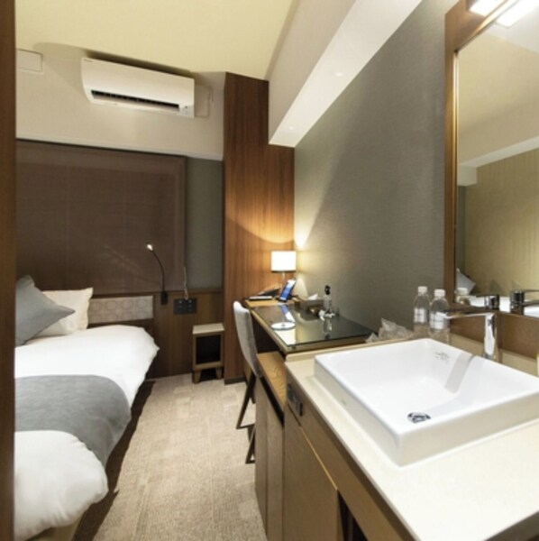 Une chambre d’hôtel comprenant un lit, un bureau, un grand miroir et une salle de bain avec un lavabo et des toilettes.