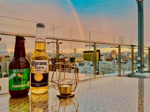 Eine Flasche Corona Extra und eine Flasche Craft Beer auf einer Dachterrasse mit Blick auf die Stadt.