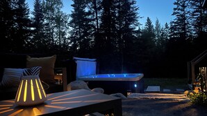 A hot tub surrounded by a deck with a lamp and a chair. - La Cache à Théo (Lac-Supérieur)
