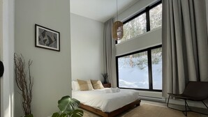 A modern bedroom with a large window, a bed, a chair, and a plant. - La Cache à Théo (Lac-Supérieur)