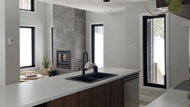 A modern kitchen with a large island, dark wood cabinets, and a sleek black faucet. - La Cache à Théo (Lac-Supérieur)