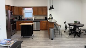 A modern kitchen with wooden cabinets, a stainless steel refrigerator, a built-in oven, a dishwasher, and a small dining area with a round table and chairs. - Modern 3BR & 2BA Near McCormick & Downtown (Chicago)