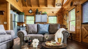 A cozy log cabin interior with a sofa, two coffee tables, and a dining table set with food and drinks. - Stunning Fall Colors From Double Decks, 15 min to Gatlinburg, Firepit, HotTub (Sevierville)
