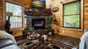 A cozy cabin interior with a stone fireplace, wooden walls, and a television mounted above it. - Stunning Fall Colors From Double Decks, 15 min to Gatlinburg, Firepit, HotTub (Sevierville)