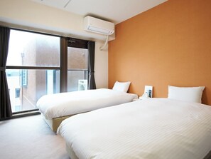 A hotel room with two beds, an air conditioning unit, a window with curtains, and a view of buildings outside.