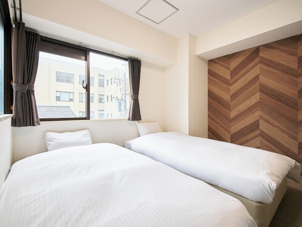 Une chambre d’hôtel avec deux lits, une grande fenêtre avec des rideaux et un mur orné d’un motif en chevrons.