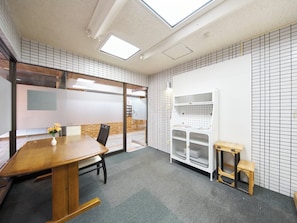 A meeting room with a wooden table, chairs, a white shelving unit, and a glass partition.