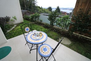A patio with a round table and chairs, a small garden area, and a view of a body of water.
