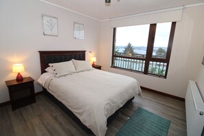 A bedroom with a bed, two bedside lamps, a window with a view, and a radiator.