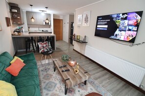 A living room with a green sofa, a wooden coffee table, and a television mounted on the wall displaying a movie selection.