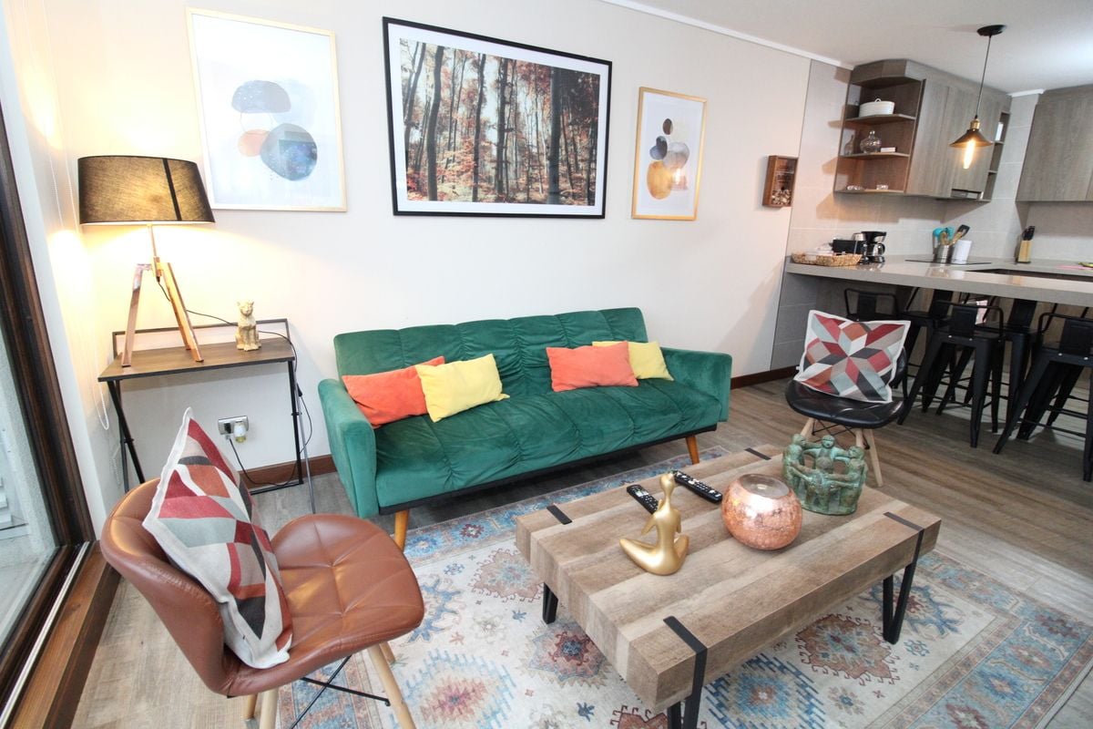 Un salon avec un canapé vert, une table basse et une lampe. Il y a également un coin cuisine avec un bar et des chaises.