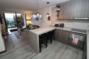 A modern kitchen with a central island, bar stools, a built-in oven, and a dining area with a sofa and table.