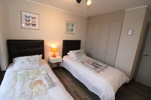 A hotel room with two beds, a nightstand with a lamp, and a wardrobe.